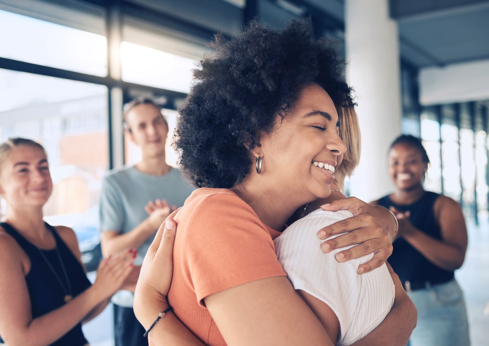 A young woman embracing a friend, surrounded by smiling supporters